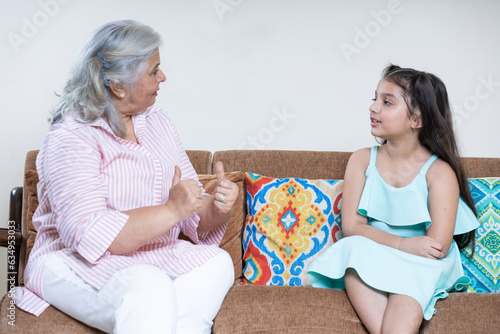 Indian grandmother and Granddaughter having conversation together in living room sitting together on sofa, Family unity concept
