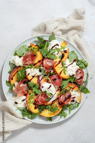 Healthy summer salad with peach, burrata, arugula and jamon
