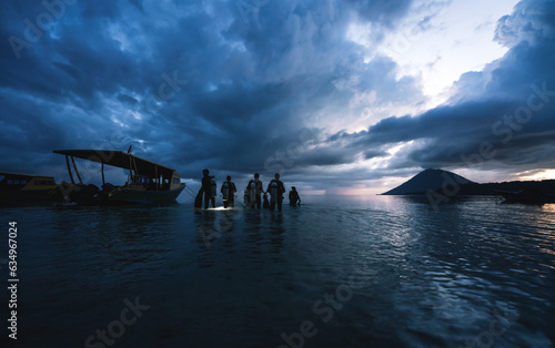 Divers walking into the ocean during sunset for a night dive in Bunaken, Sulawesi, Indonesia