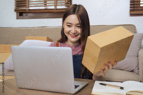Young business woman working online e-commerce shopping at home. Young woman seller prepare parcel box of product for deliver to customer