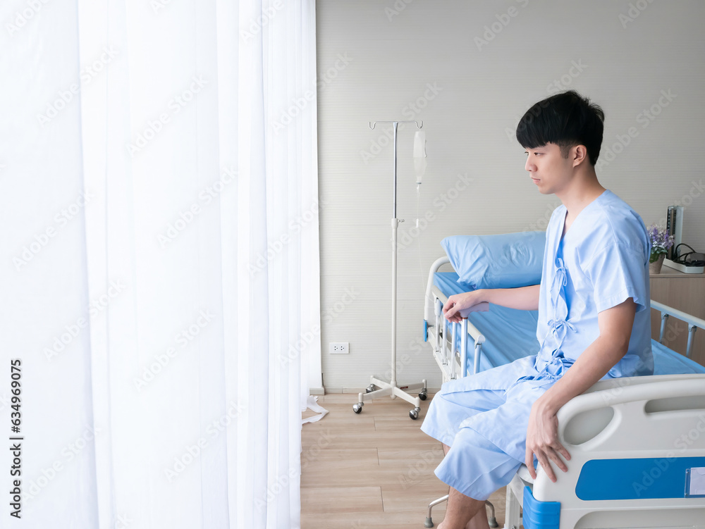 Asian patient man sitting with absent minded when he know about disease diagnosis in hospital bed near curtain window in the private room while wearing inpatient uniform Asian patient man sitting with absent minded when he know about disease diagnosis in hospital bed near curtain window in the private room while wearing inpatient uniform