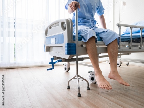 Patient male holding tripod cane while sitting in hospital bed for support body and help walking when he stand on a floor in recovery room