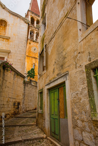 A street of historic stone houses in Milna Village on Brac Island in Croatia with traditional kogule or kogulavanje paving. The bell tower of Church of Our Lady of the Annunciation is in background