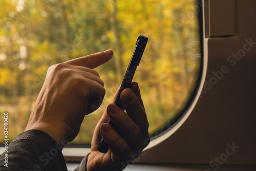 Close-up shot of woman's hands tapping on mobile phone screen Female traveler in high speed train autumn outside. Unrecognizable woman Scrolling social media on mobile phone. Using technologies while