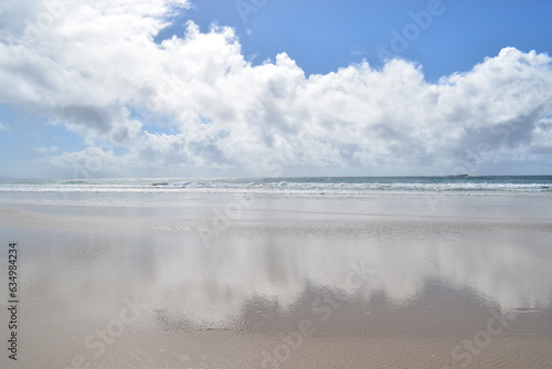 reflections of clouds in wet sand on a sunny beach