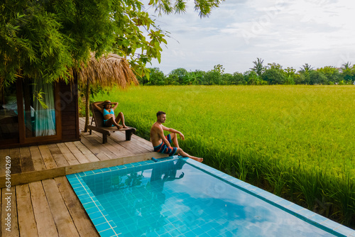 a couple of men and women in front of a Bamboo hut homestay farm, with Green rice paddy fields in Central Thailand with a small plunge pool looking out over green rice paddy fields