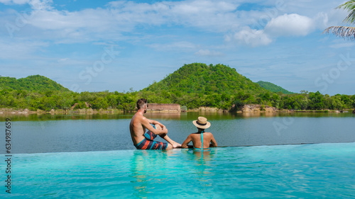 couple on the edge of a swimming pool on vacation in Thailand looking out over the lake and green mountains of Central Thailand.  © Fokke Baarssen