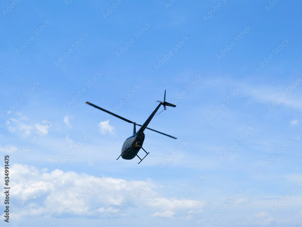 Black helicopter in flight. A small private helicopter against a blue sky and white clouds. Black helicopter in flight. A small private helicopter against a blue sky and white clouds.