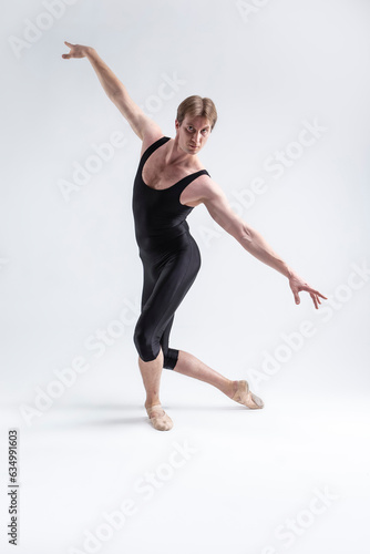 Sports Concepts and Ideas. Young Athletic Caucasian Ballet Dancer Man Posing in Stretching Pose With Hands Lifted in Line and Knees Bended in Black Tights On White.