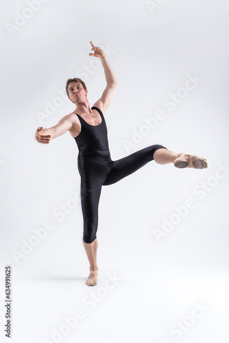Sports Ideas. Athletic Caucasian Ballet Dancer Man Posing in Dancing Stretching Pose With Hands Lifted Up in While Standing on Feet in Black Tights On White. © danmorgan12