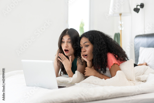 Young asian LGBT Lesbian couples are using laptops to search for information to buy a new home. while embracing each other in bed.