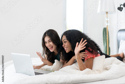 Young asian LGBT Lesbian couples are using laptops to search for information to buy a new home. while embracing each other in bed.