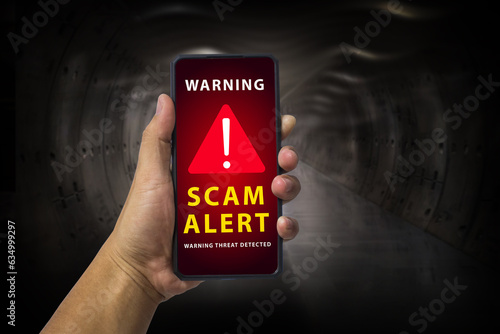 Man hand holding a mobile phone with red screen and warning icon with the text "SCAM ALERT", Security mobile concept, security risk.