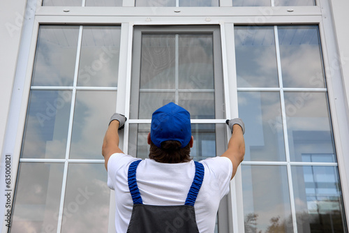 Professional craftsman outside the building installs a mosquito net on large window that lifts it up. Installation of protective net on white plastic window in summer