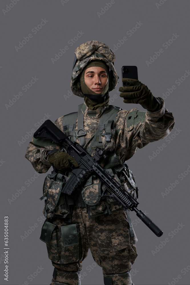 Military man with a gun and a mobile phone takes a selfie or has a video chat, showing a casual and modern side of a soldier's life Military man with a gun and a mobile phone takes a selfie or has a video chat, showing a casual and modern side of a soldier's life