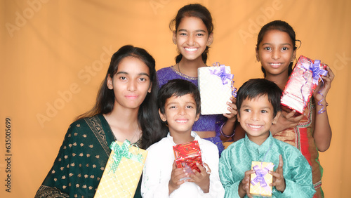 Happy young indian kids exchange gift box celebrating diwali festival together isolated on studio background. brother give present to sister.