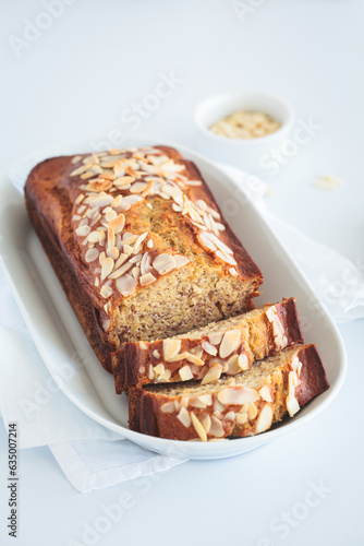 Banana bread with almonds on a white plate on white background.