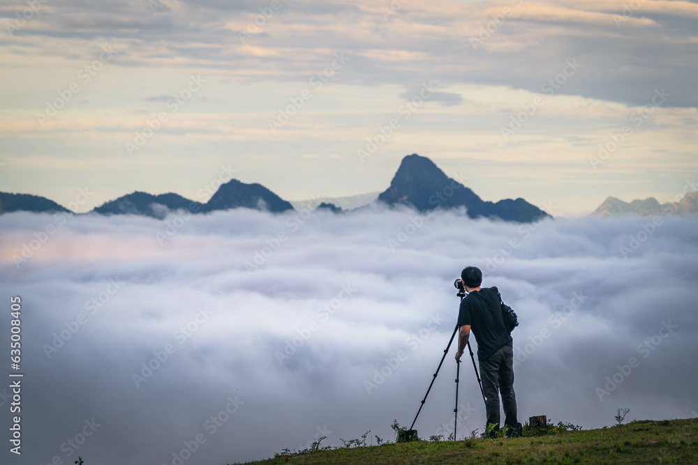 A man with tripod taking a photo in the mountain summit with sea of cloud, fantastic sky and sunrise (Tak province, Thailand)