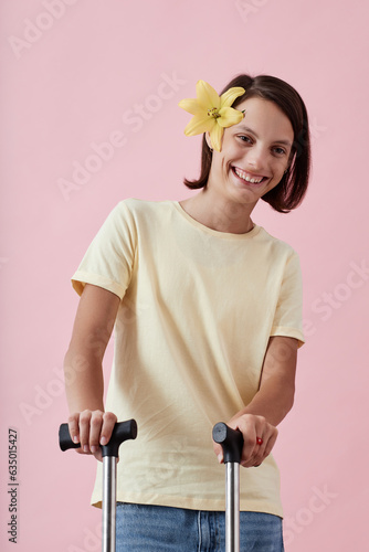 Vertical portrait of smiling teen girl with cerebral palsy posing holding crutches against pink background in studio