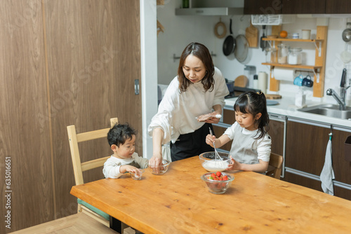 春の昼間の自宅のキッチンでケーキ作りをする日本人の女の子とその手伝いをする母親と弟