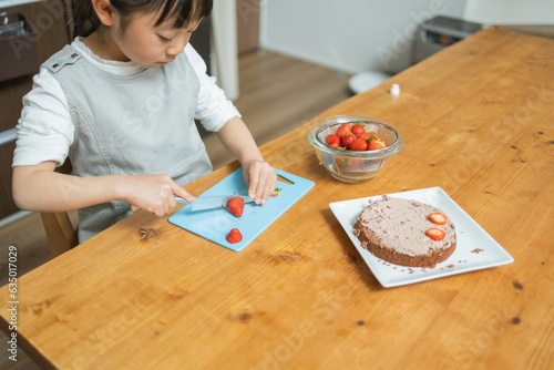 春の日中に屋内のテーブルでケーキに乗せる苺を切る日本人の女子 photo