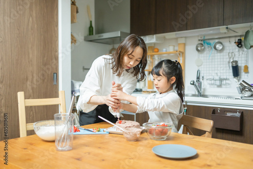 春の昼間に家の台所のテーブルで2人で一緒に誕生日のケーキ作りをする日本人の親子