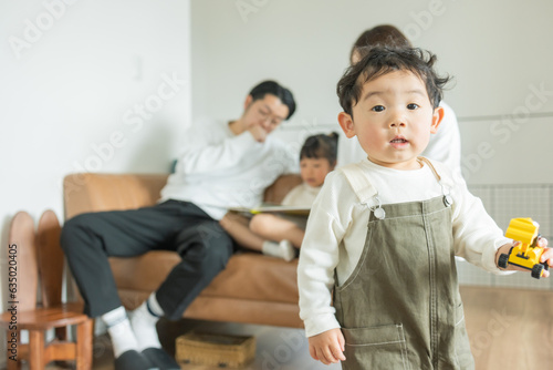 春に家の部屋でおもちゃの車を持って立つ小さい日本人の子供とその家族 photo