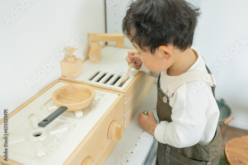 春の日中のこども部屋でおままごとのキッチンで下を向いて料理の真似をする日本人の幼児 photo