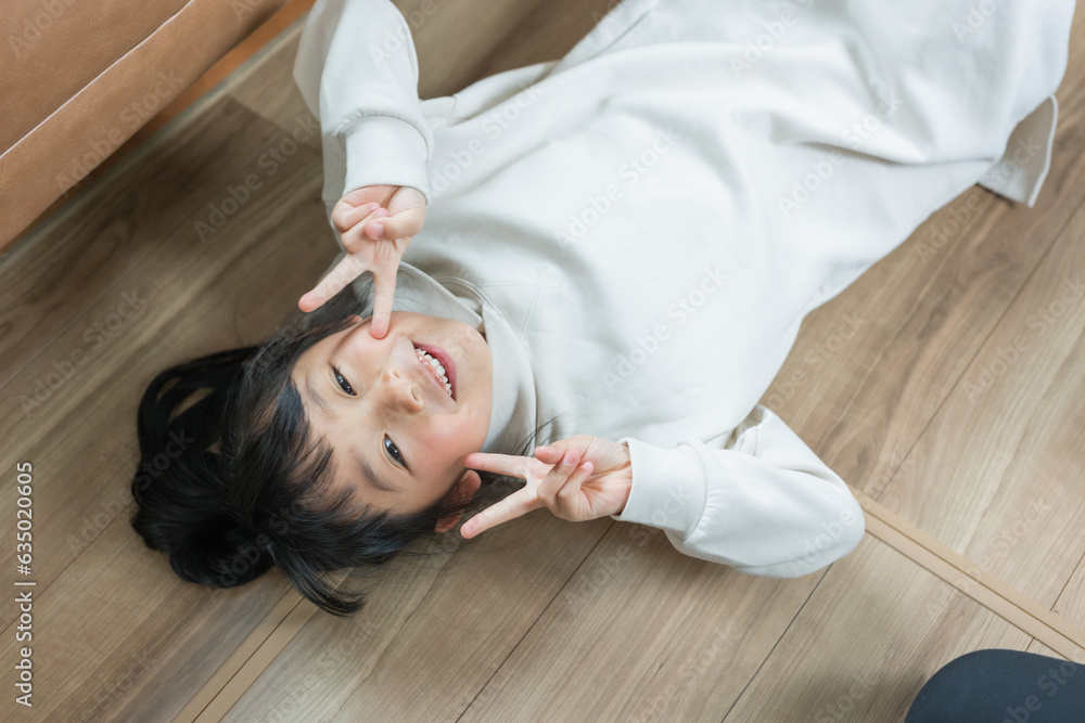 Φωτογραφία 春の昼間、床に寝転んで両手でピースをして笑うアジア人の小学生の子ども