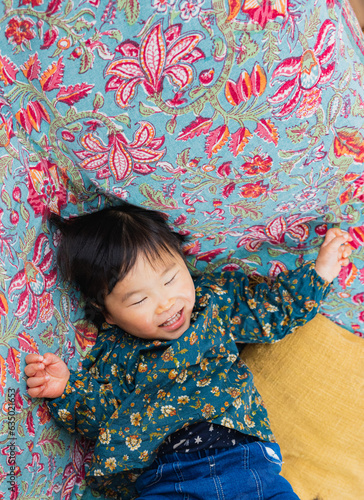 春の昼間、リビングの花柄ソファの上で楽しそうに寝転ぶ日本人の黒髪の女の子