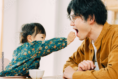 春の午後、部屋で口を開けて娘にお菓子を食べさせてもらう日本人の父親 photo