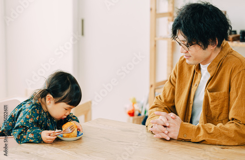 春の昼間、椅子に座っておやつを食べる日本人の女の子と見つめる男性 photo