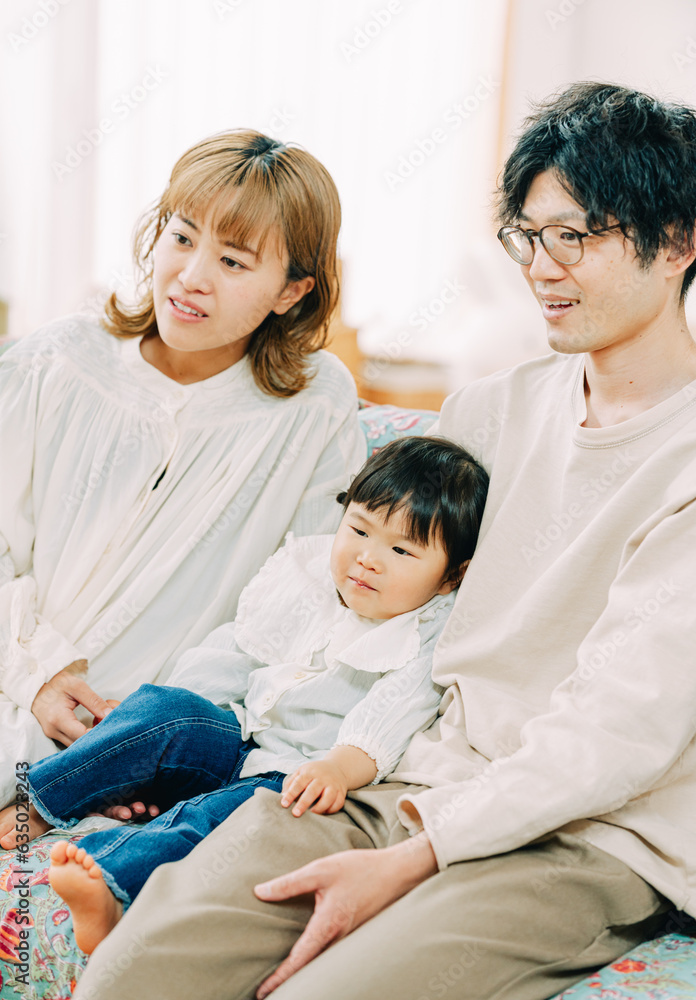 春の日中、家でソファに座って笑顔で前を見つめるアジア人の家族 春の日中、家でソファに座って笑顔で前を見つめるアジア人の家族
