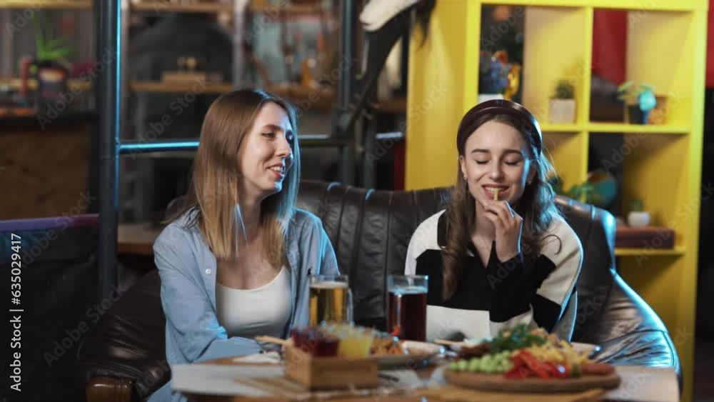 Young girls are sitting in a restaurant with lots of food on the table. They are in good spirits, chatting and eating happily. They are talking very emotionally. Young girls are sitting in a restaurant with lots of food on the table. They are in good spirits, chatting and eating happily. They are talking very emotionally.