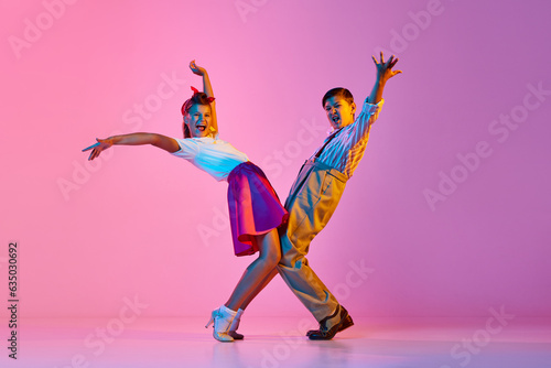 Talented, artisitc children, boy and girl in retro clothes dancing lindy hop against pink studio background in neon light. Concept of childhood, hobby, active lifestyle, performance, art, fashion photo