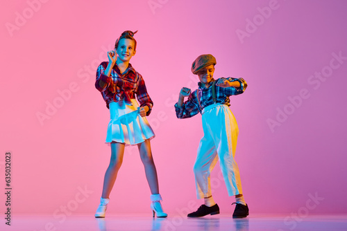 Canvas Print Stylish, emotional children in retro clothes dancing lindy hop against pink studio background in neon light