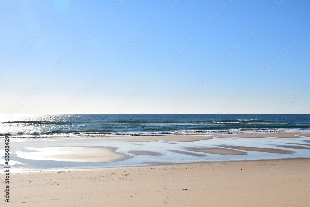 Deserted natural beach with sun reflections, calm blue sea, cloudless blue sky and clear horizon, usable as seaside background with space for a message, Manta Rota, Algarve, Portugal
