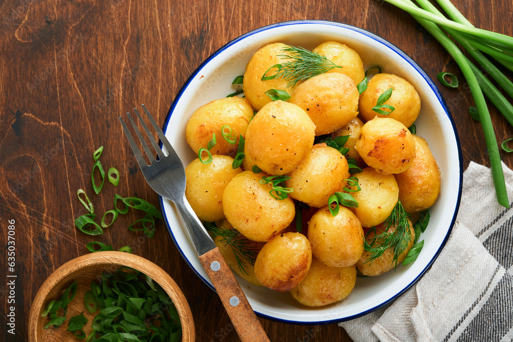 Boiled new or young potatoes with butter, fresh dill and onions in white bowl on dark old rustic wooden background. Tasty new boiled potatoes. Top view. Boiled new or young potatoes with butter, fresh dill and onions in white bowl on dark old rustic wooden background. Tasty new boiled potatoes. Top view.