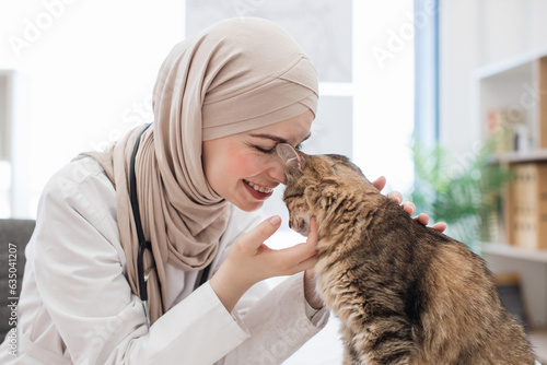 Fototapeta Naklejka Na Ścianę i Meble -  Vet in hijab fondling furry patient in exam room of clinic