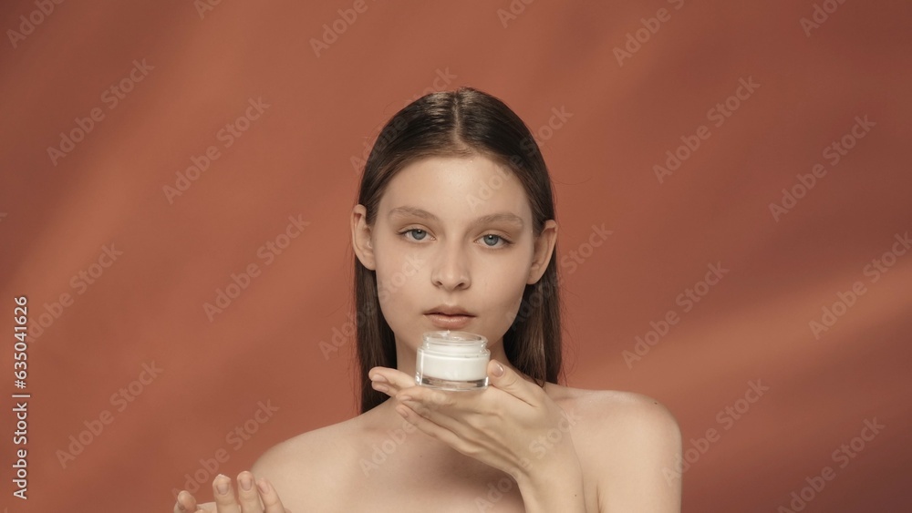 A woman holds a jar of cosmetic cream. Seminude woman with a jar of cream in the studio on a red background. The concept of beauty, cosmetology, care. A woman holds a jar of cosmetic cream. Seminude woman with a jar of cream in the studio on a red background. The concept of beauty, cosmetology, care.