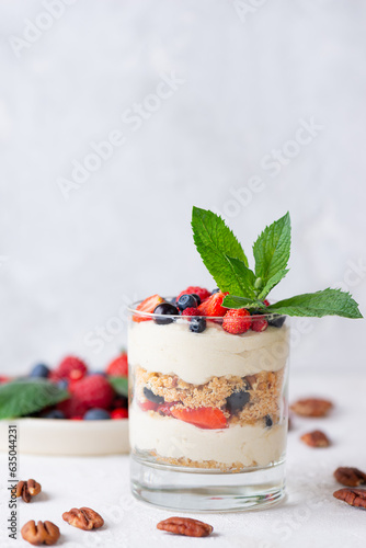 Sweet dessert in a glasses with berries, mint, nuts, whipped cream and biscuit. Vegan, sugar, gluten and lactose free.