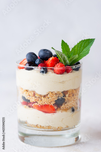 Cold dessert in a glasses with berries, mint, nuts, whipped cream and biscuit. Healthy food, vegan, sugar, gluten and lactose free.