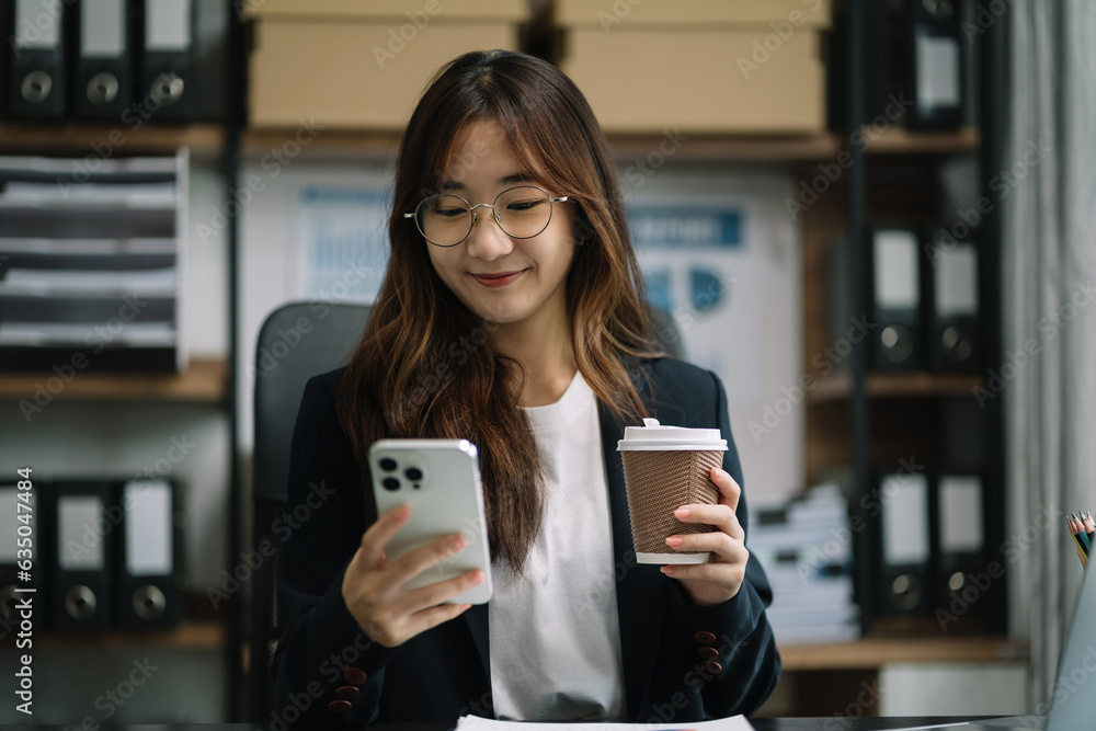 Asian businesswoman sits in a office working on smartphone and enjoys a coffee. Asian businesswoman sits in a office working on smartphone and enjoys a coffee.