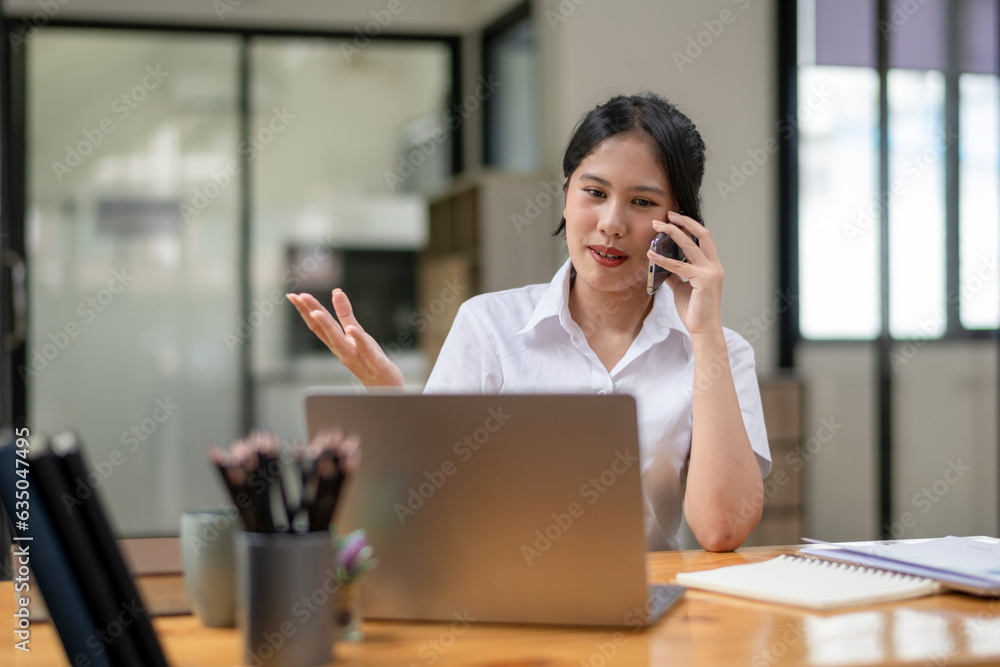 Happy female trainee talking on the phone while working on laptop Happy female trainee talking on the phone while working on laptop