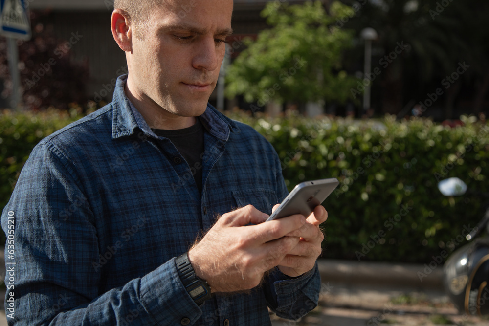 A middle-aged Caucasian man, looks at his smartphone to consult some information, on the street, on a sunny day A middle-aged Caucasian man, looks at his smartphone to consult some information, on the street, on a sunny day