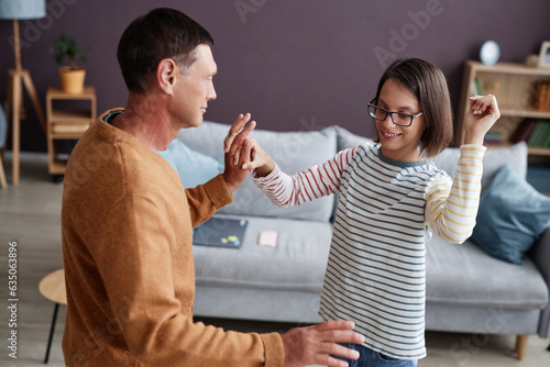 Portrait of smiling teenage girl with cerebral palsy dancing with father in home interior photo