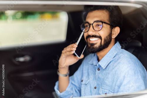 Indian man sitting on car back seat, talking on phone