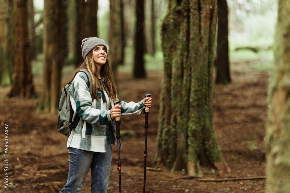 Happy young caucasian woman in jacket with trekking sticks walk enjoy trip alone in forest Happy young caucasian woman in jacket with trekking sticks walk enjoy trip alone in forest