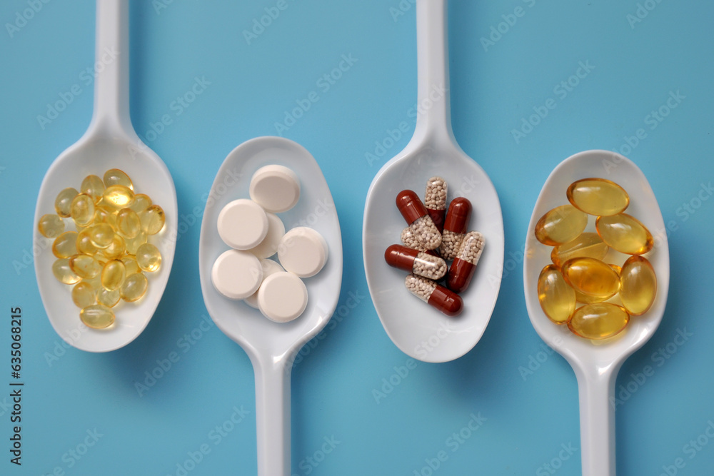 Tablets, capsules, dietary supplements, vitamins on white spoons. Medical background with pills - obrazy, fototapety, plakaty 
