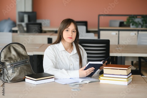 Teen girl studying with textbook writing essay learning in classroom.